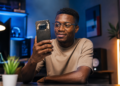 Jeune homme africain utilisant un Nothing Phone (4a) dans un environnement high-tech moderne, avec éclairage cinématique et design transparent caractéristique du smartphone.