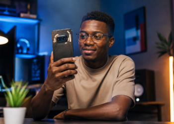 Jeune homme africain utilisant un Nothing Phone (4a) dans un environnement high-tech moderne, avec éclairage cinématique et design transparent caractéristique du smartphone.