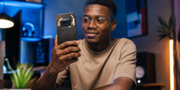 Jeune homme africain utilisant un Nothing Phone (4a) dans un environnement high-tech moderne, avec éclairage cinématique et design transparent caractéristique du smartphone.