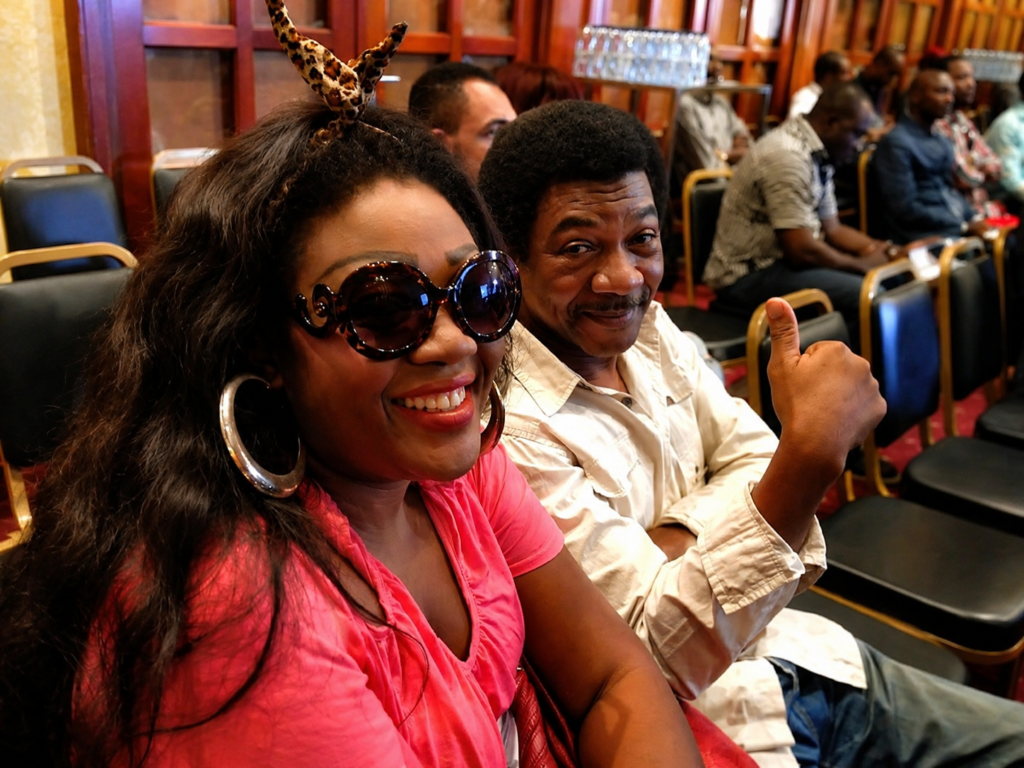 Foly Dirane et son épouse Tatiana Dirane souriant lors d'un événement public au Cameroun, dans une salle de conférence.