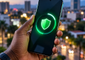 Smartphone Android tenu par une main noire, affichant un bouclier vert symbolisant la protection des données et les mises à jour de sécurité, sur fond urbain flouté.