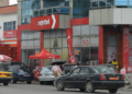 Façade d’un bâtiment aux couleurs de Nexttel Cameroun, avec l’enseigne de l’opérateur mobile, des véhicules stationnés et des installations commerciales.