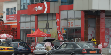 Façade d’un bâtiment aux couleurs de Nexttel Cameroun, avec l’enseigne de l’opérateur mobile, des véhicules stationnés et des installations commerciales.